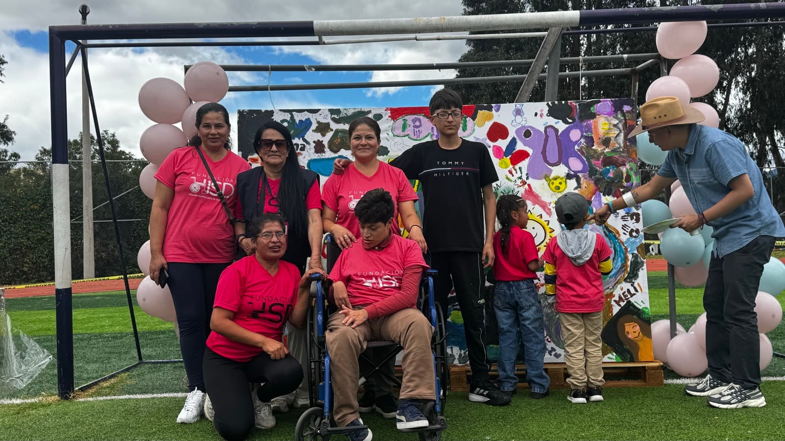 Grupo de niños, madres y voluntarios de Fundación HSD junto a un mural pintado en un evento